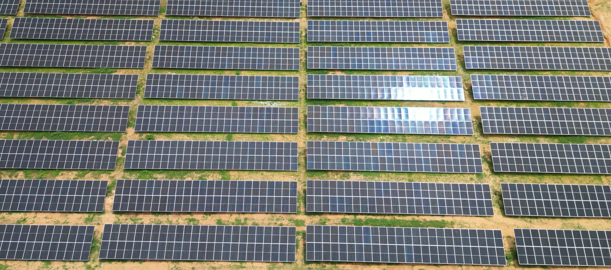 Aerial view of long rows of solar panel tables laid out across red soil at the Pavagada site